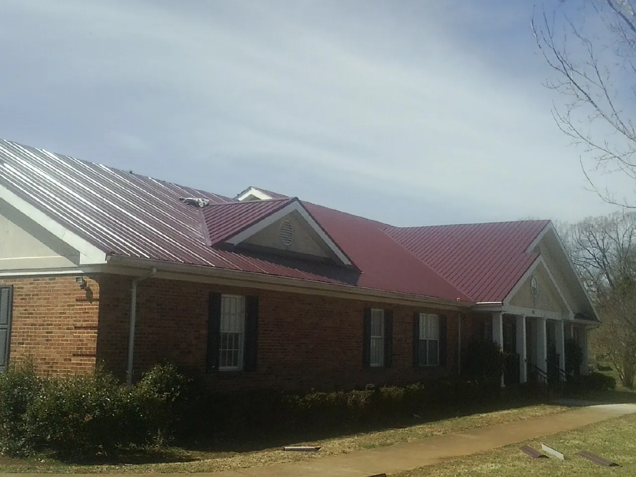 Red metal roof with gabled entries on a long brick building, from a Hail Damage Roof Repair job in Mc Clure