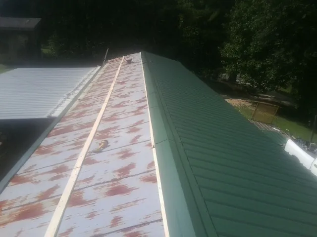 Old rusted panels beside newly installed green metal roofing — Wind Damage Roof Repair by Roofing Brothers in Mc Clure